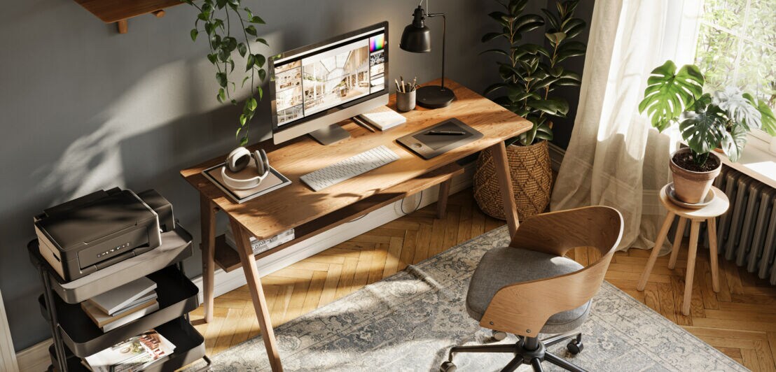 Helles Home-Office mit Holztisch, Computer, Pflanzen und einem Stuhl auf einem gemusterten Teppich vor einem Fenster mit weißen Vorhängen