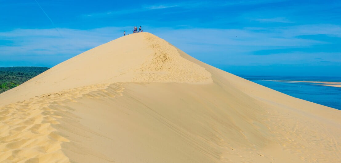 Menschen stehen auf der Spitze einer großen Sanddüne unter blauem Himmel