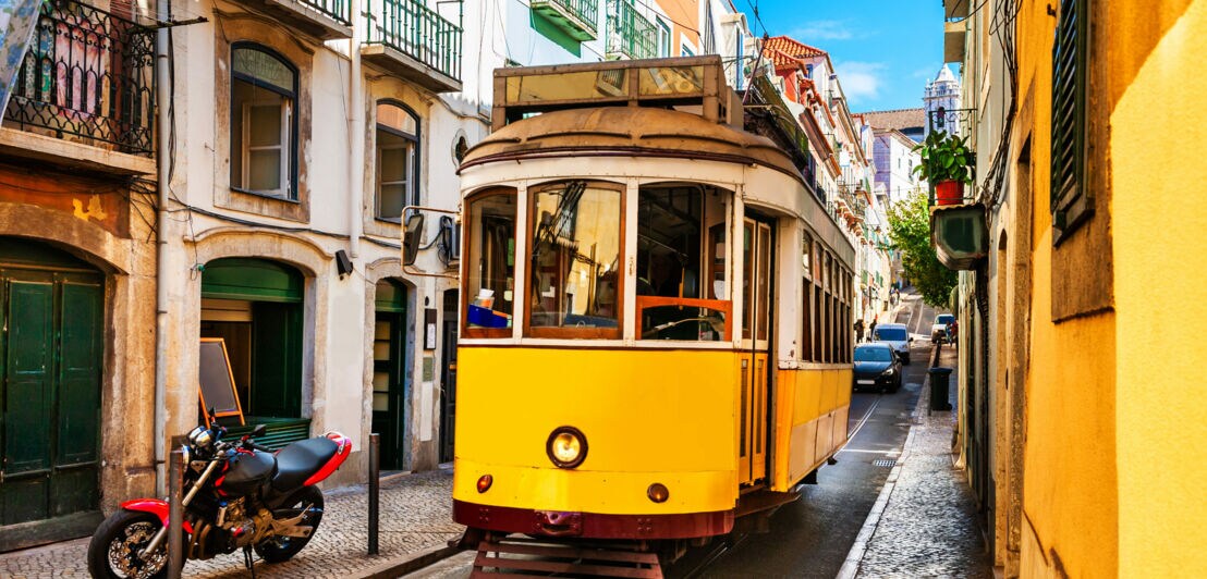 Gelbe historische Straßenbahn fährt durch enge Gasse mit mehrstöckigen Häusern in Lissabon