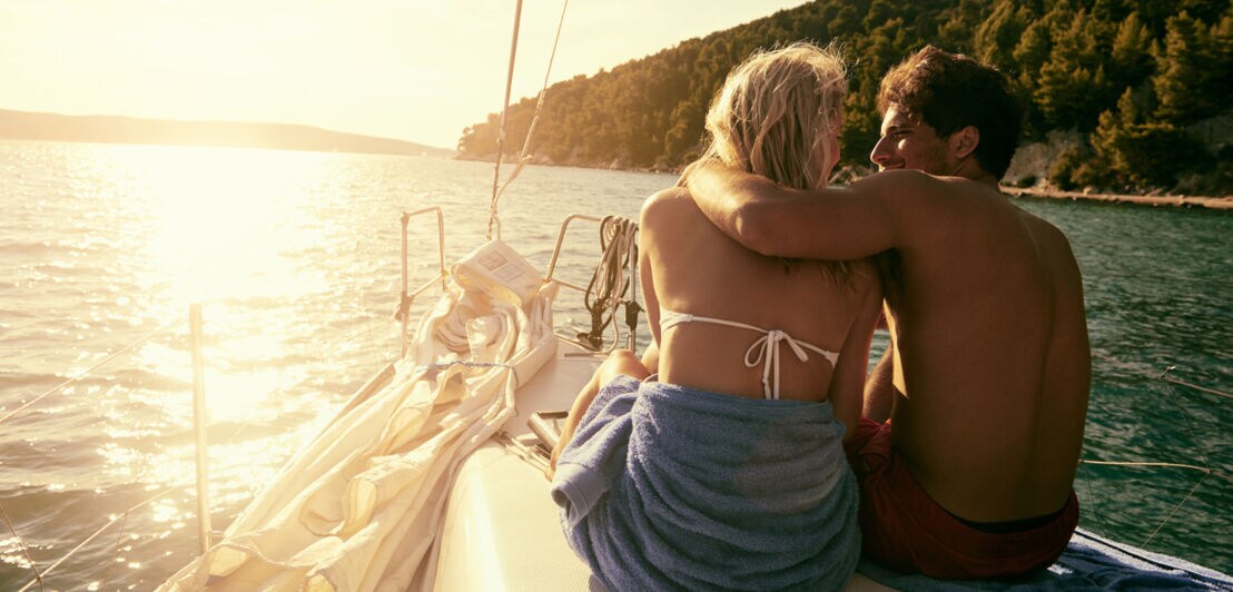 Paar sitzt eng umschlungen auf einem Boot bei Sonnenuntergang, umgeben von Wasser und bewaldeten Hügeln