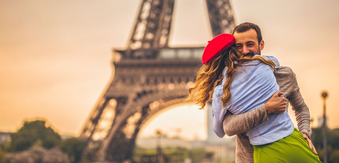 Paar umarmt sich glücklich vor dem Eiffelturm bei Sonnenuntergang in Paris