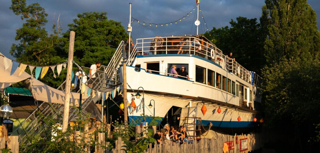 Alte Utting, ein stillgelegtes Passagierschiff auf einer Brücke im Schlachthofviertel München, mit Menschen an Deck und Dekoration