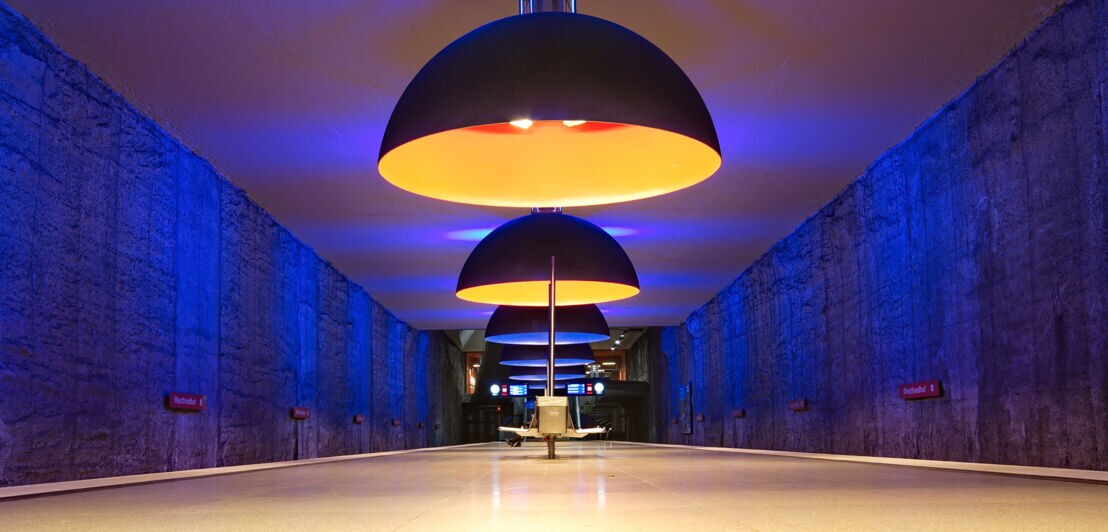 Drei große, runde Pendelleuchten hängen über einem langen, leeren Flur mit blauen Wänden