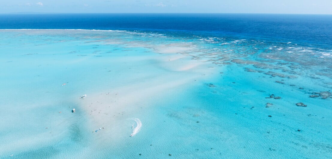 Luftaufnahme einer weißen Sandbank mit Booten und Personen im türkisblauen Meer.