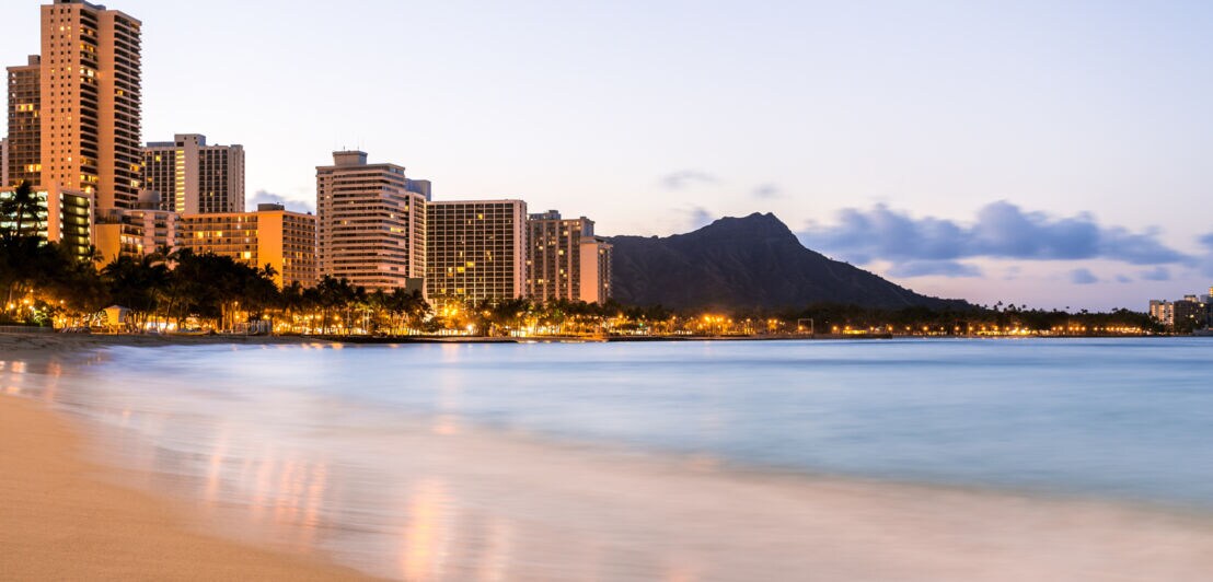 Skyline des Waikiki Beachs bei Sonnenaufgang, mit hohen Hotels und dem Diamond Head.