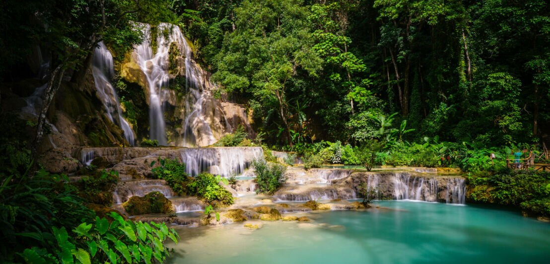 Mehrstufiger Wasserfall fließt in einen türkisfarbenen natürlichen Pool, umgeben von dichtem grünen Wald
