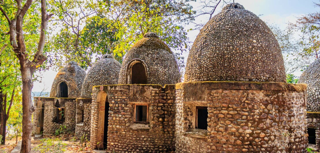 Vier kuppelförmige Gebäude aus kleinen Steinen in einem bewaldeten Gebiet