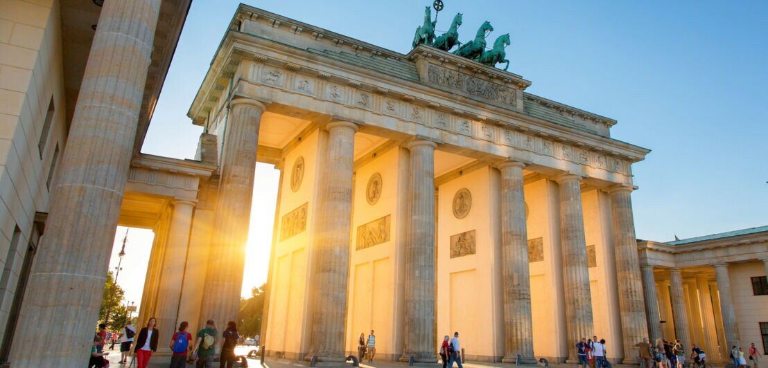 Personen am Brandenburger Tor, durch das Sonnenstrahlen scheinen.