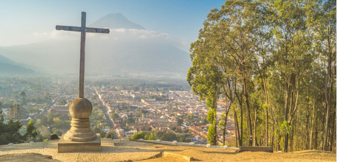 Holzkreuz auf einem Hügel mit Blick auf eine Stadt und einen Berg im Hintergrund