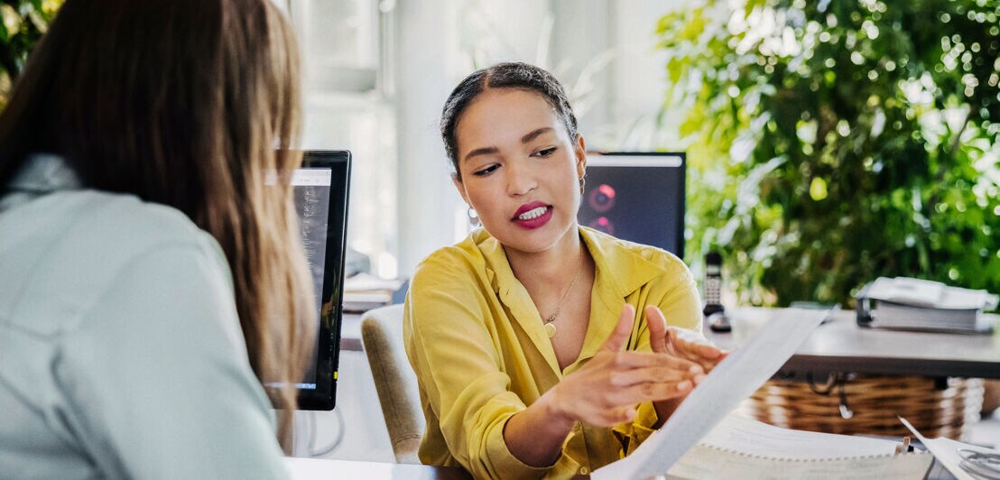 Eine weibliche Führungskraft bespricht sich im Büro mit einer Mitarbeiterin.
