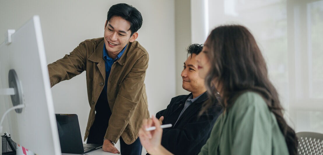 Ein junger Mitarbeiter erklärt seinen Kolleg:innen etwas am Bildschirm.