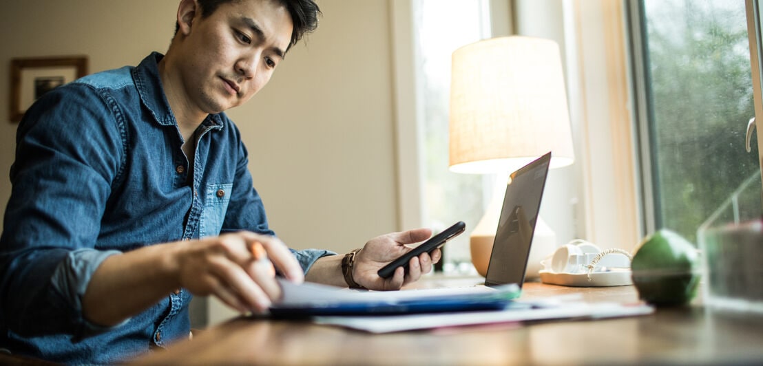 Ein Mann erledigt die Buchhaltung mit Smartphone und Laptop.