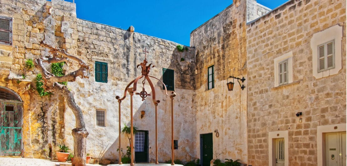 Innenhof eines historischen Steinhauses mit einem alten Brunnen in der Mitte und blauem Himmel