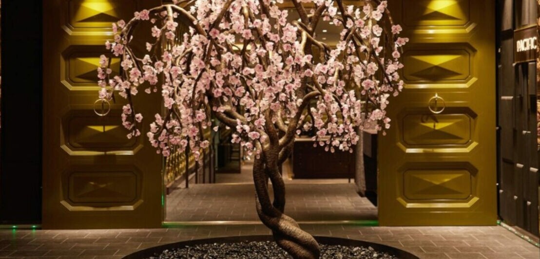 Skulptur in Baumform mit rosa Blüten in einem Rondell in einem eleganten Foyer.