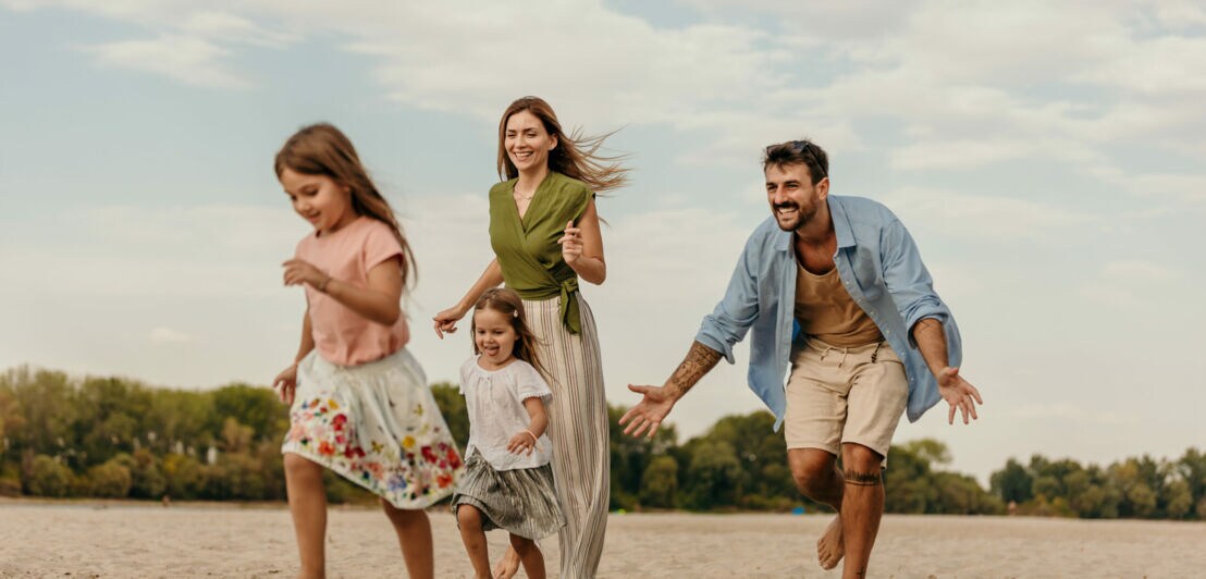 Eine Frau und ein Mann und zwei Kinder laufen barfuß am Strand.