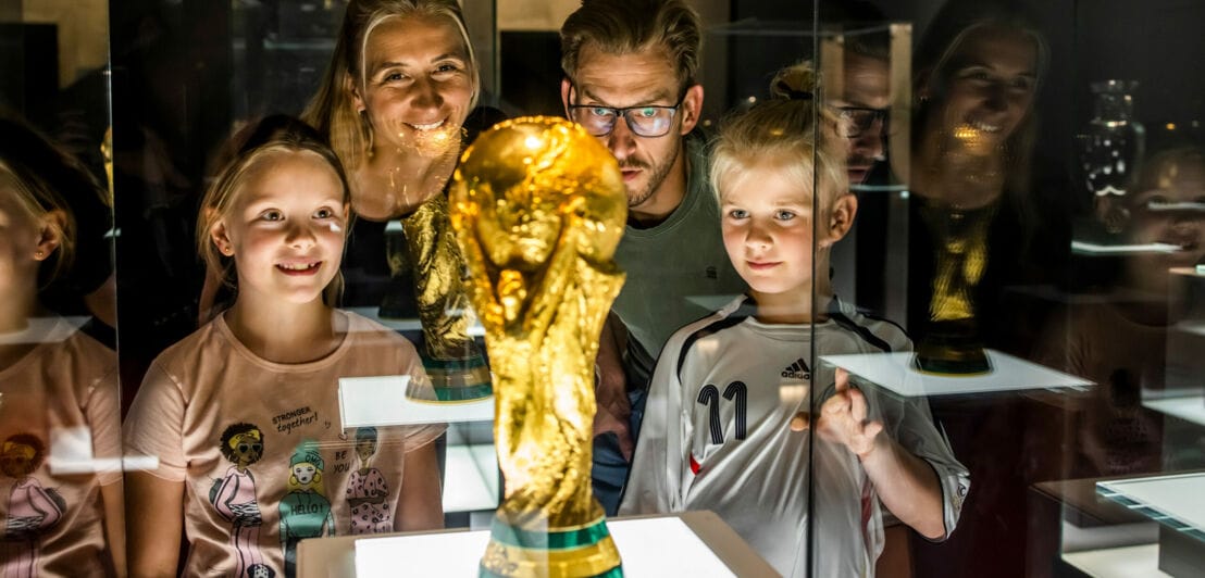 Eltern mit Kindern stehen um den FIFA-Weltmeisterschaftspokal in einer Vitrine im Museum Schatzkammer