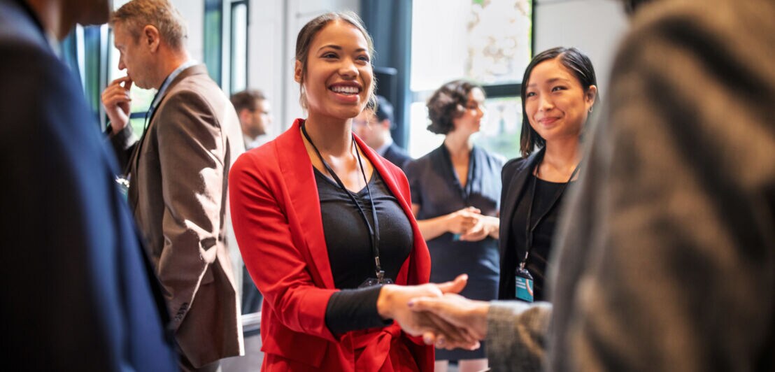 Eine Versammlung von Menschen, bei der eine Frau in rotem Anzug einer Person die Hand gibt.