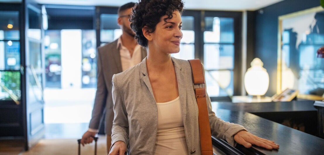 Eine Frau und ein Mann mit Rollkoffern an einer Hotelrezeption.