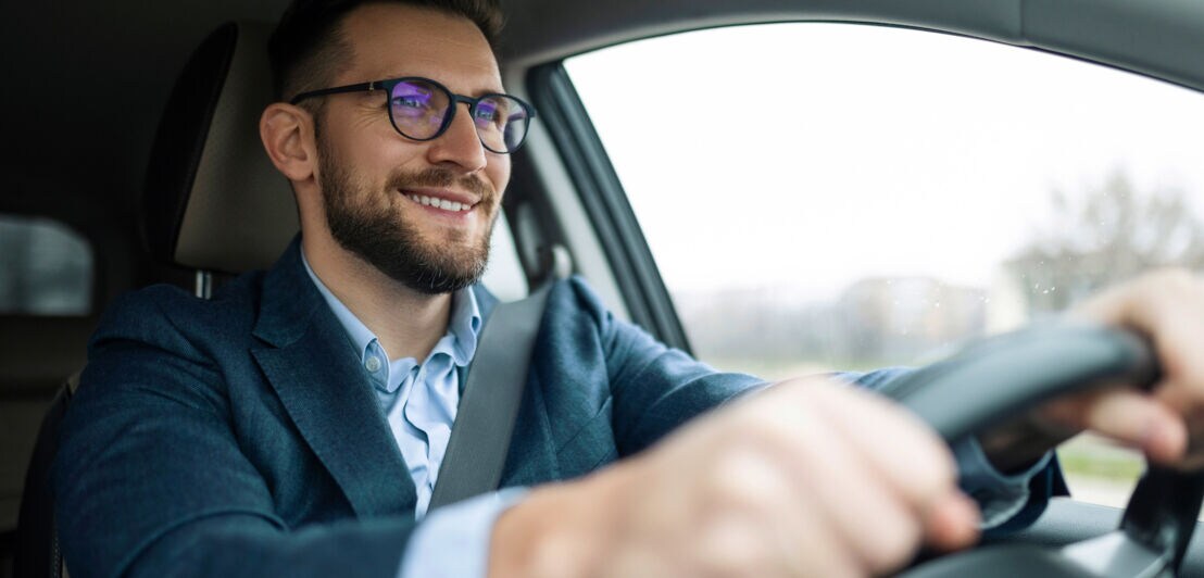 Ein Mann im Business-Outfit fährt lächelnd Auto.