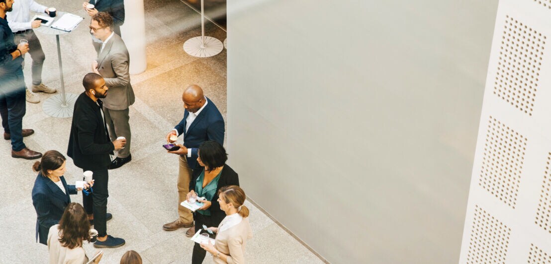 Eine Gruppe Geschäftsleute diskutiert rund um Stehtische.