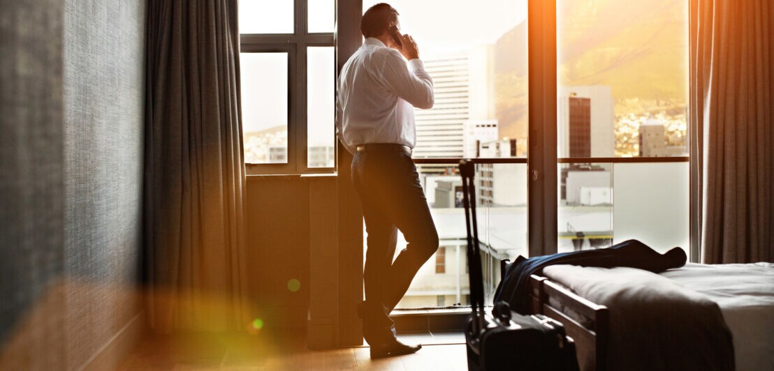 Geschäftsmann steht am Fenster eines Hotelzimmers und telefoniert.