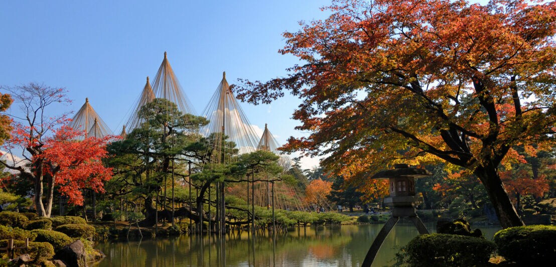 Herbstliche Landschaft im Kenrokuen-Garten mit Kotoji-Laterne am Teich und bunt gefärbten Bäumen