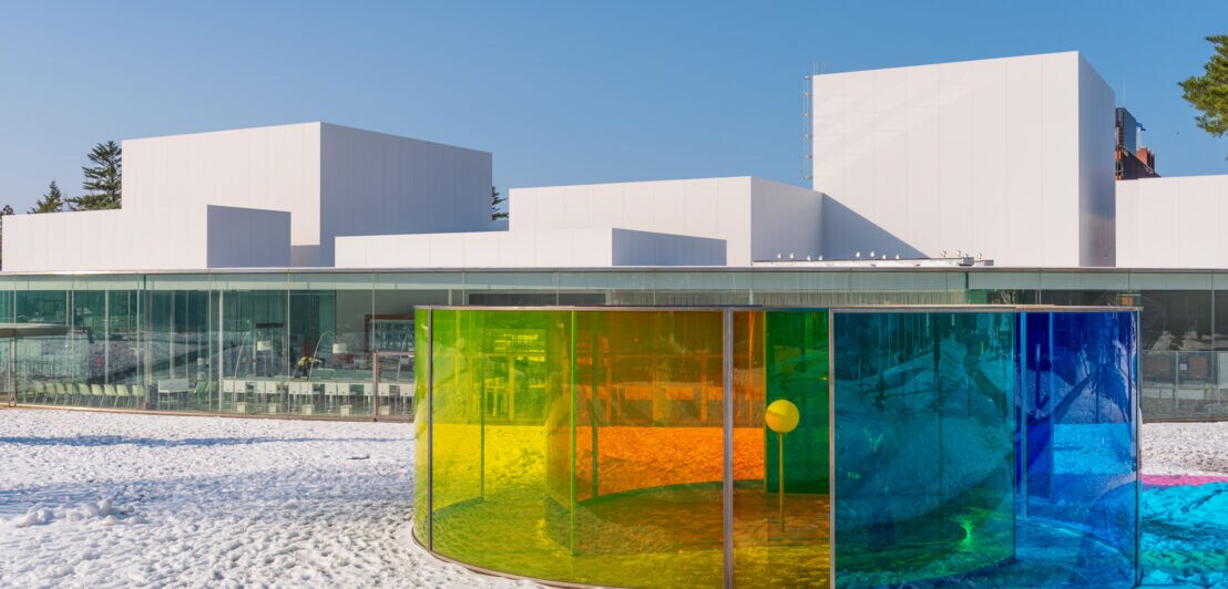 Modernes weißes Gebäude mit flachem Dach hinter einem kreisförmigen Pavillon aus farbigem Glas im Schnee