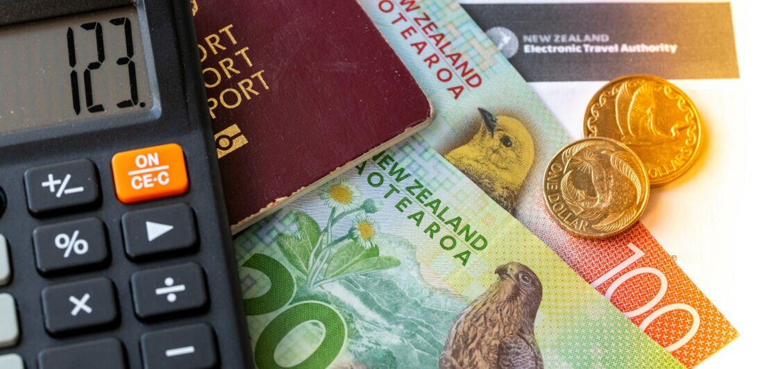 Close-up des NZeTA-Formulars, auf dem neuseeländisches Geld, ein Reisepass sowie ein Taschenrechner liegen.