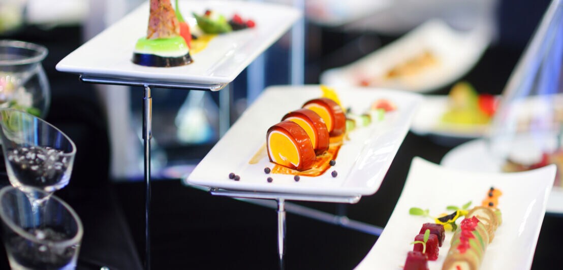 Verschiedene kunstvoll angerichtete Gourmet-Häppchen auf weißen rechteckigen Tellern bei einem Buffet