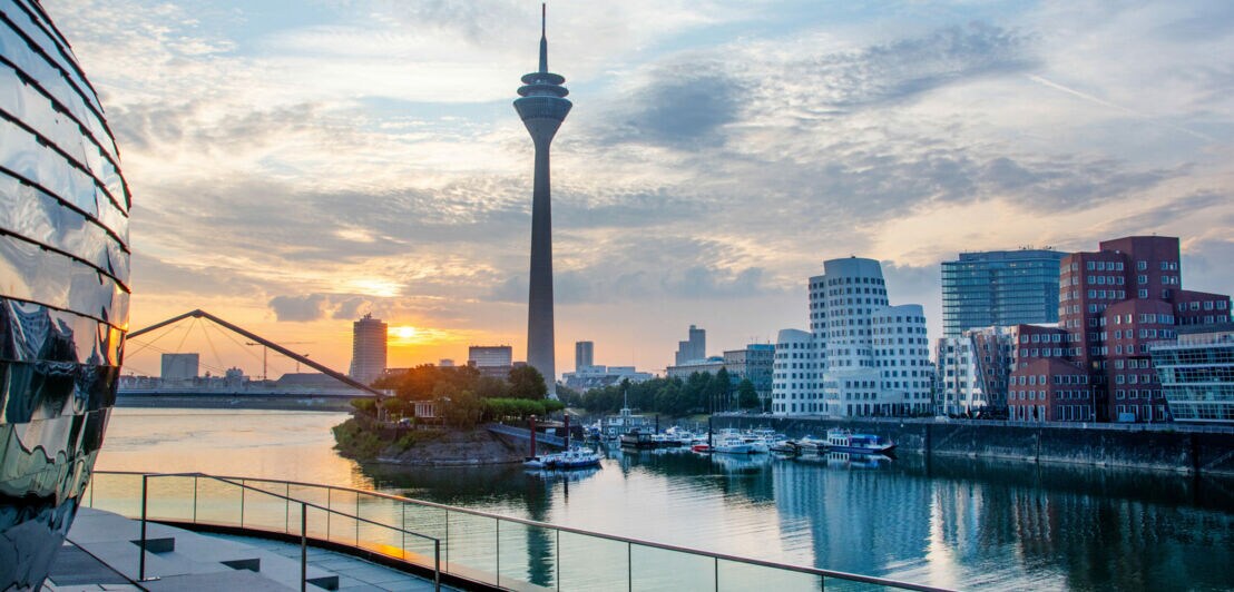 Blick auf den Rheinturm und die MedienHafen-Gebäude in Düsseldorf bei Sonnenuntergang mit Hafenbecken im Vordergrund