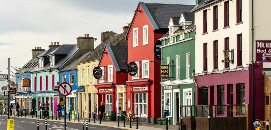 Bunte Häuserzeile mit roten, grünen und blauen Fassaden, Straßenszenen mit Verkehrsschildern und Laternen, irische Architektur.