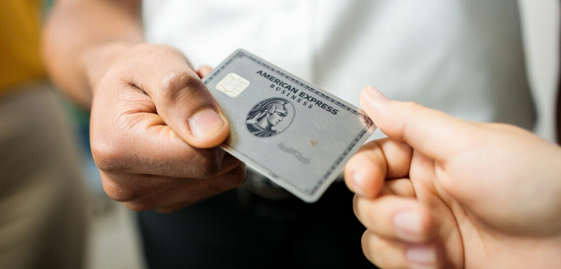 Eine Person übergibt einer anderen eine Business Platinum Card von American Express.