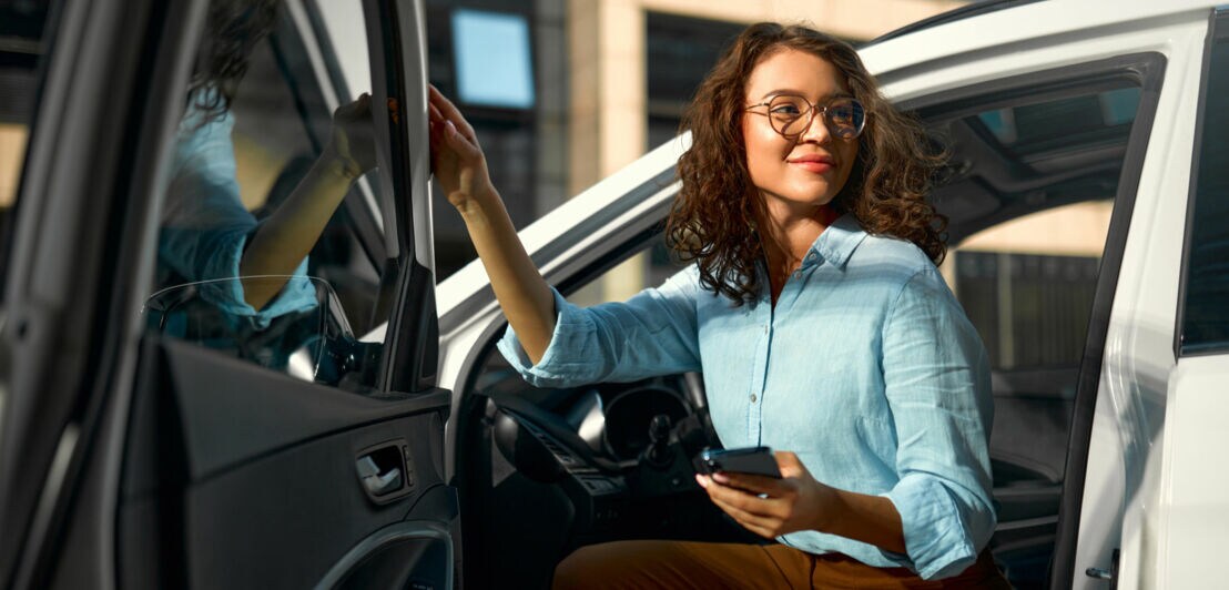 Eine junge Frau mit Smartphone in der Hand steigt aus einem Auto.
