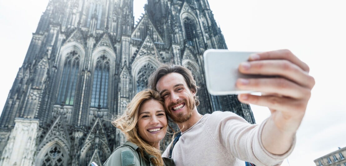Ein Mann und eine Frau machen ein Selfie vor dem gotischen Kölner Dom.