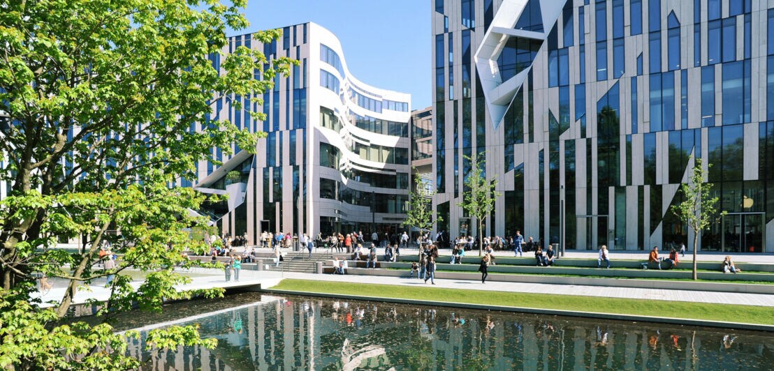 Moderne Bürogebäude mit Glasfassaden am Wasserbecken im Kö-Bogen Düsseldorf, Menschen sitzen und gehen auf der Promenade.