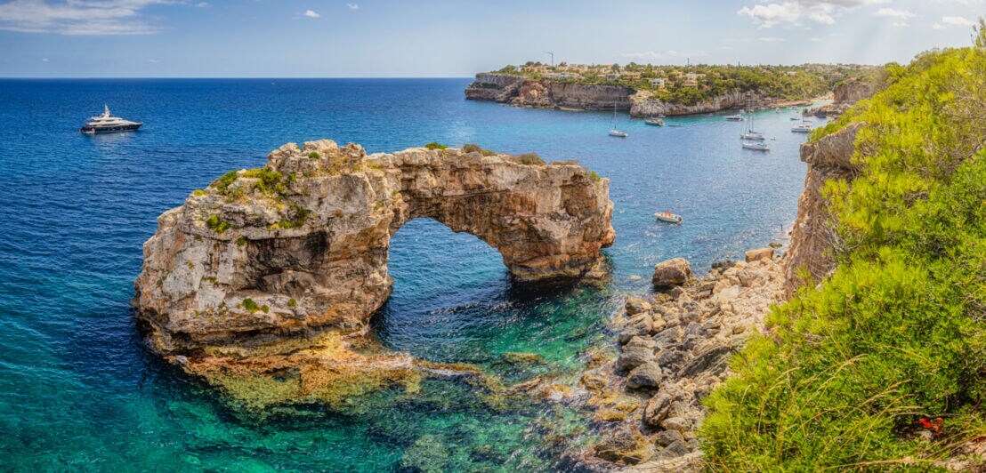 Natürlicher Felsenbogen über klarem blauem Meerwasser an der Küste mit mehreren Booten und bewachsenen Klippen