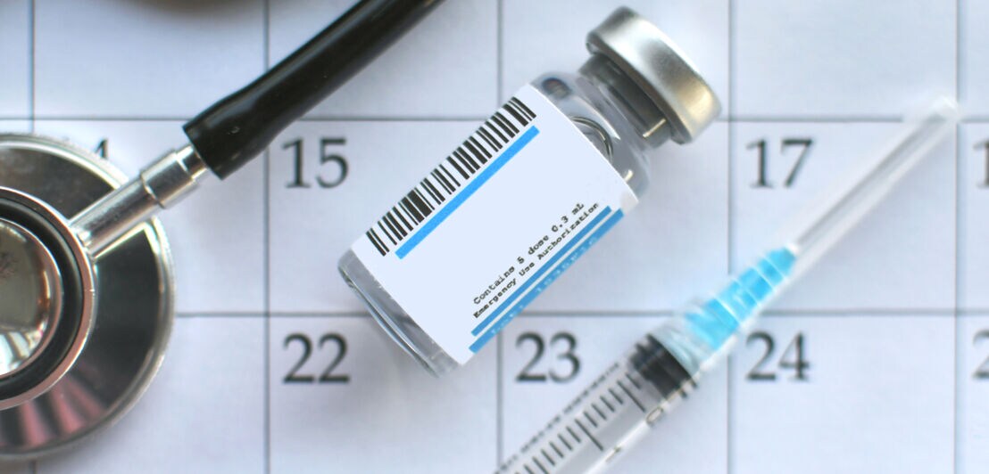 Impfstofffläschchen mit Barcode, Spritze und Stethoskop auf einem Kalenderblatt mit den Tagen 15 bis 23 sichtbar