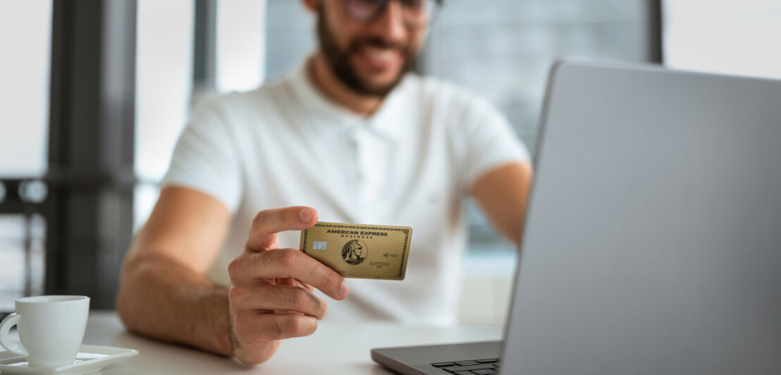 Eine Person vor einem Laptop hält eine Business Gold Card von American Express in der Hand.