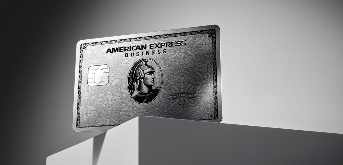 Nahaufnahme einer inszenierten silberglänzenden, metallischen Business-Kreditkarte von American Express auf einem grauen Sockel vor grauem Hintergrund mit Lichtverlauf.