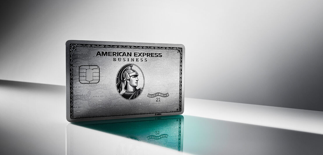 Eine aufgestellte Business Platinum Card von American Express auf einer spiegelnden Fläche vor grauem Hintergrund mit Lichtverlauf.