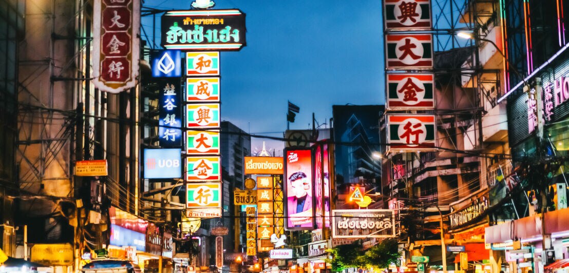 An Häusern hängen viele bunte und auffällige Leuchtreklamen, die Straßen sind voll mit Spaziergängern und Autos.