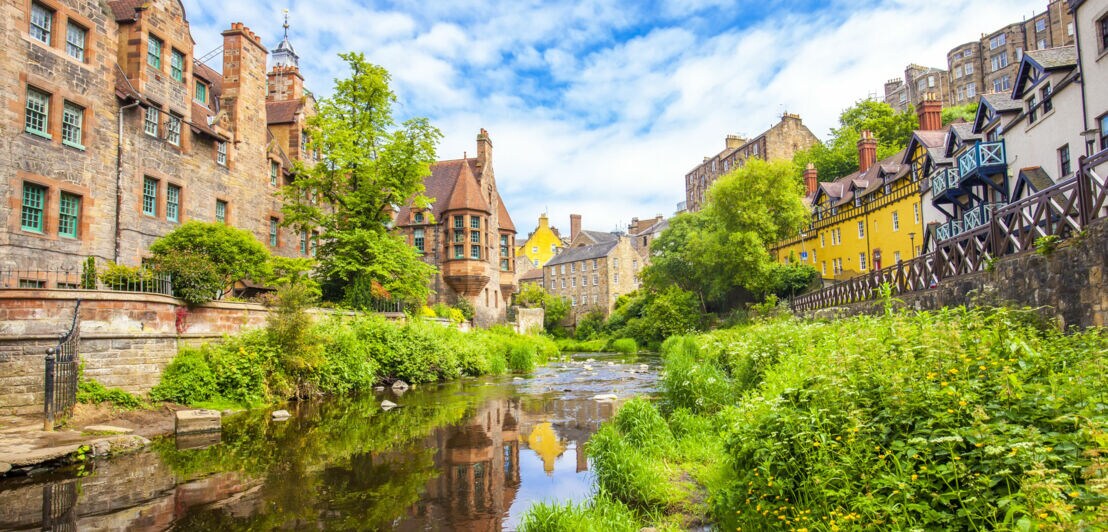 Ein schmaler Fluss, der rechts und links von alten Häusern und grünen Pflanzen gesäumt ist.