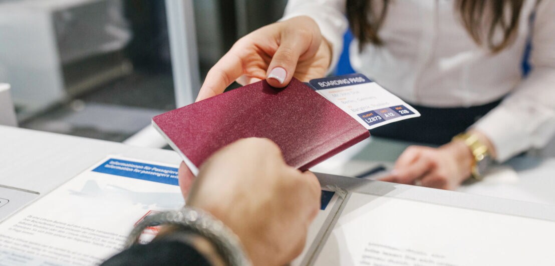 Eine Hand übergibt einen Reisepass mit Bordkarte in eine andere Hand an einem Schalter.