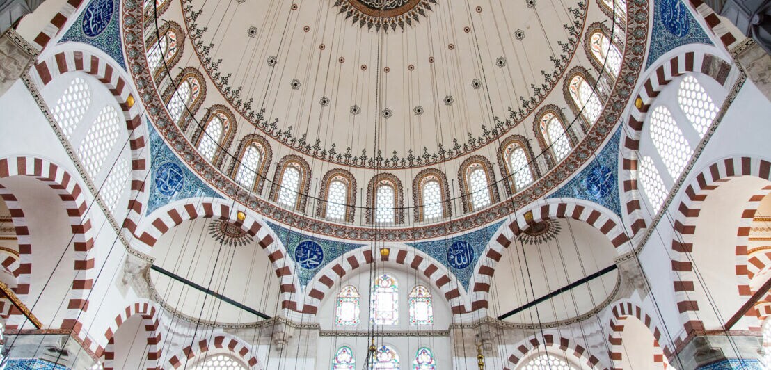 Innenansicht eines hellen Kuppeldachs einer Moschee mit blauen Kachelverzierungen.