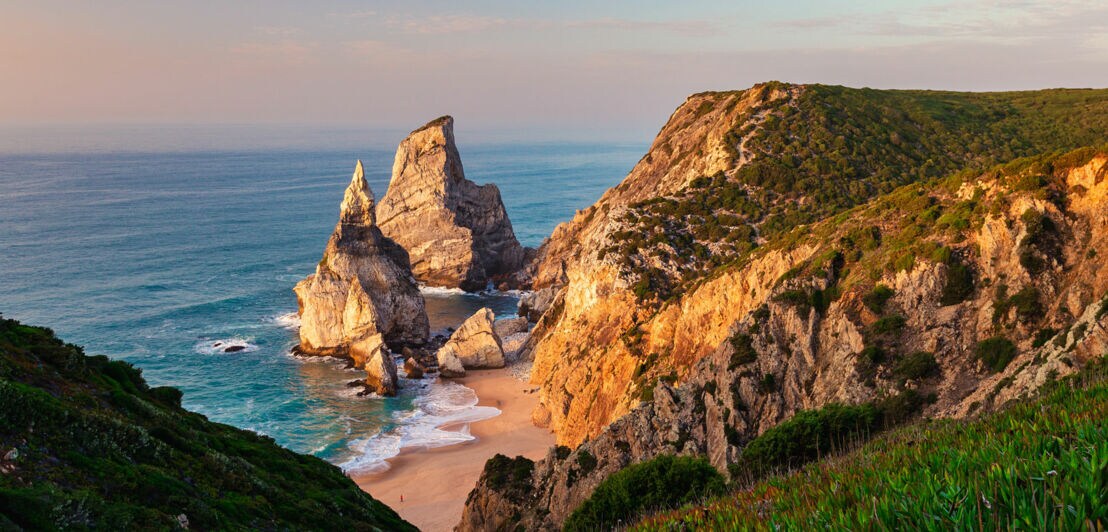 Der einsame Praia da Ursa mit seinen markanten Felsformationen von den Klippen aus und bei leichter Dämmerung in goldenem Licht.