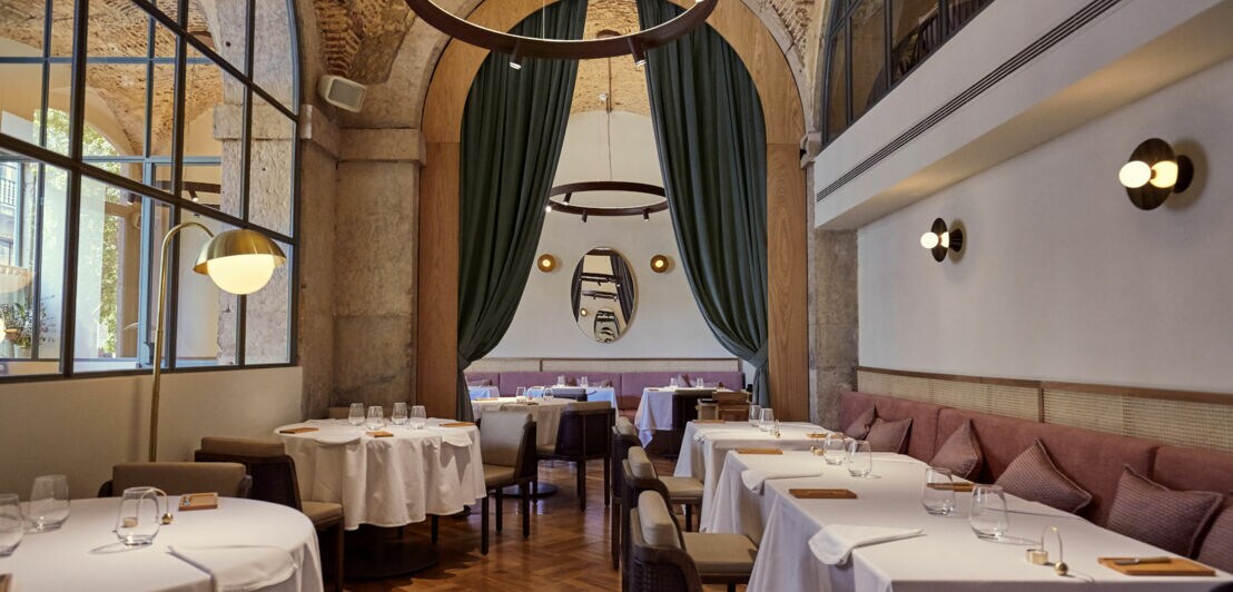 Interieur des Sternerestaurants Belcanto mit elegant eingedeckten Tischen, Designerlampen und historischem Gemäuer.