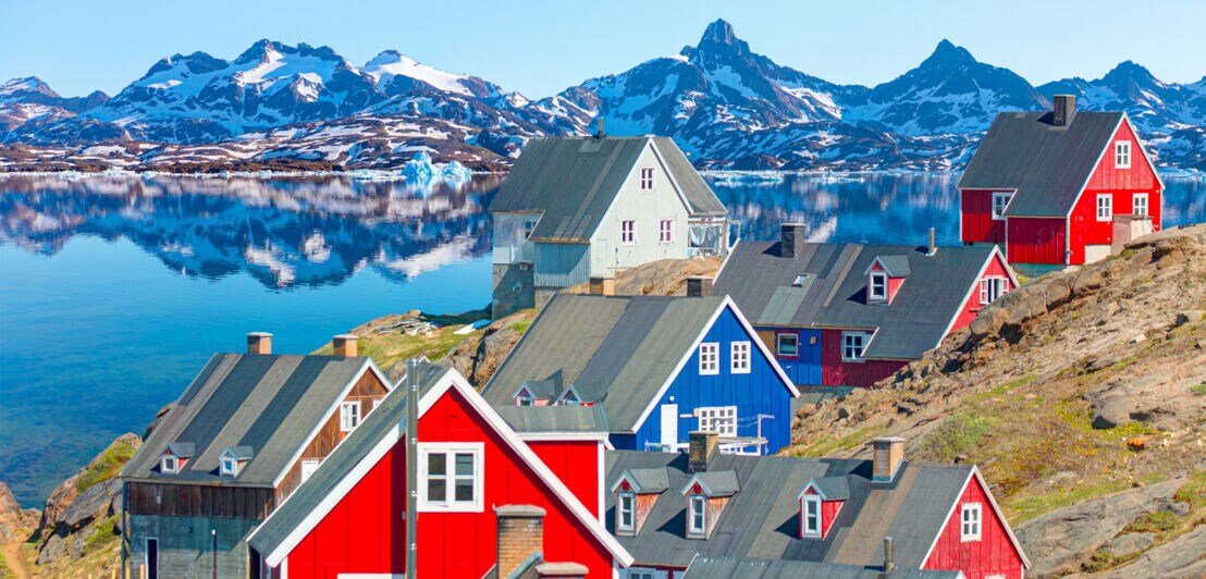 Tasiilaq im Sommer mit seinen bunten Häusern, dem klaren Fjord und den teils schneebedeckten Bergen im Hintergrund.