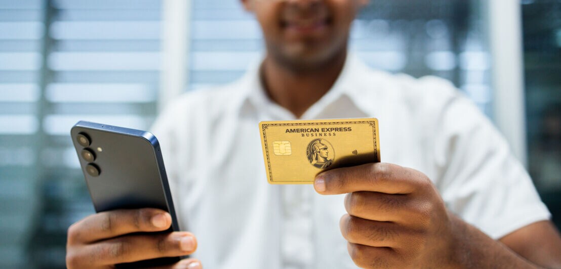 Eine Person hält in einer Hand ein Smartphone und in der anderen eine Business Gold Card von American Express.