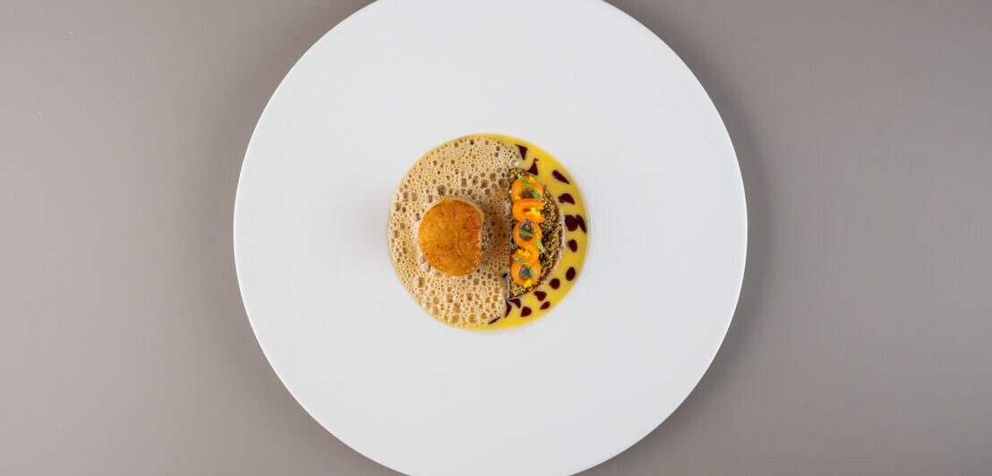 Rundes Gericht mit einer gebackenen Kugel auf Schaum, daneben gelbe Sauce mit kleinen orangefarbenen und schwarzen Tupfen auf weißem Teller, Mount Congreve Estate Gardens, Co Waterford.