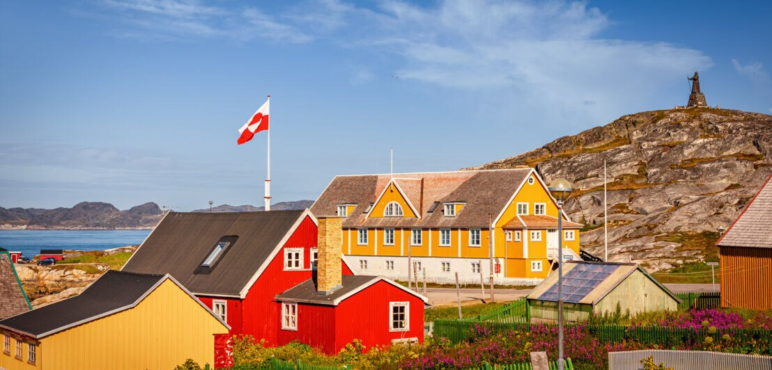 gelbe und rote Gebäude im Bereich des alten Kolonialhafens mit der Hans-Egede-Statue im Hintergrund.